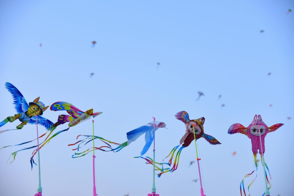 Colorful owl and bird kites flying high at a vibrant festival under a clear blue sky. Cerfs-volants en forme de hibou et d'oiseaux colorés volant haut lors d'un festival animé sous un ciel bleu dégagé.