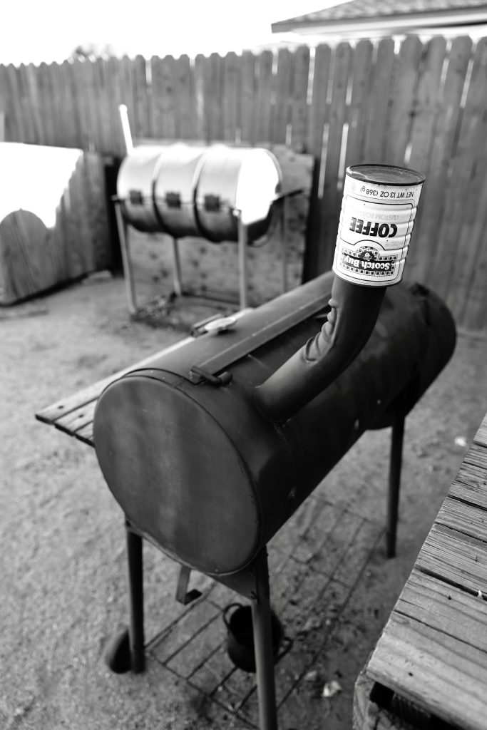 Photo en noir et blanc de barbecues et fumoirs d'extérieur dans une cour clôturée.