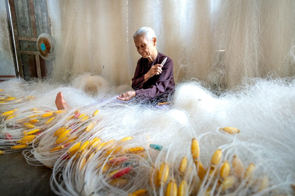 Senior woman réparant soigneusement des filets de pêche dans un cadre traditionnel