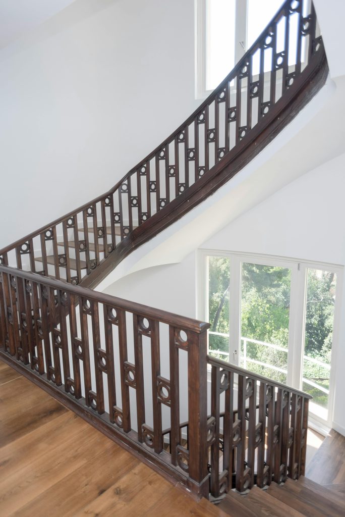 Beautiful wooden staircase with intricate railing in a sunlit interior space. Escaliers en bois magnifiques avec une rampe ouvragée dans un intérieur baigné de soleil.