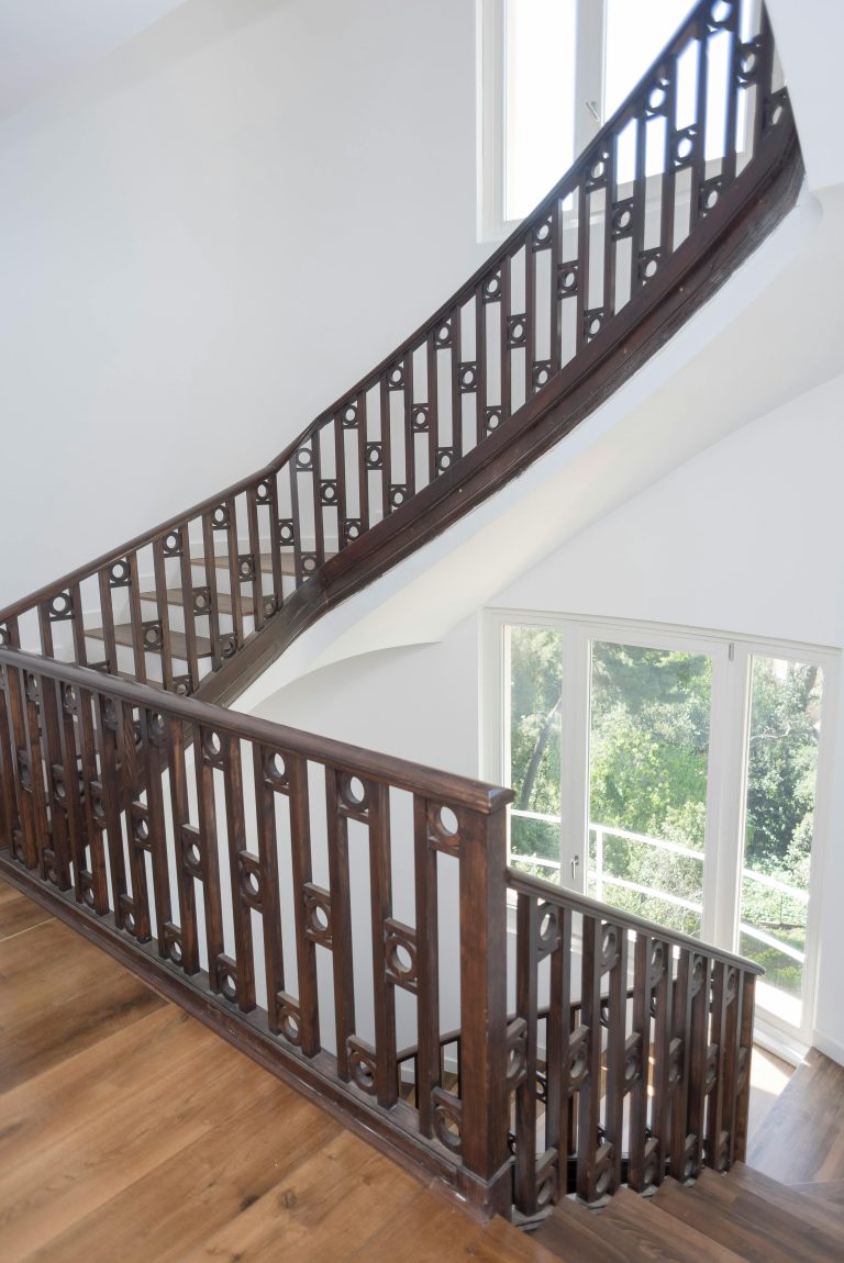 Beautiful wooden staircase with intricate railing in a sunlit interior space. Escaliers en bois magnifiques avec une rampe ouvragée dans un intérieur baigné de soleil.