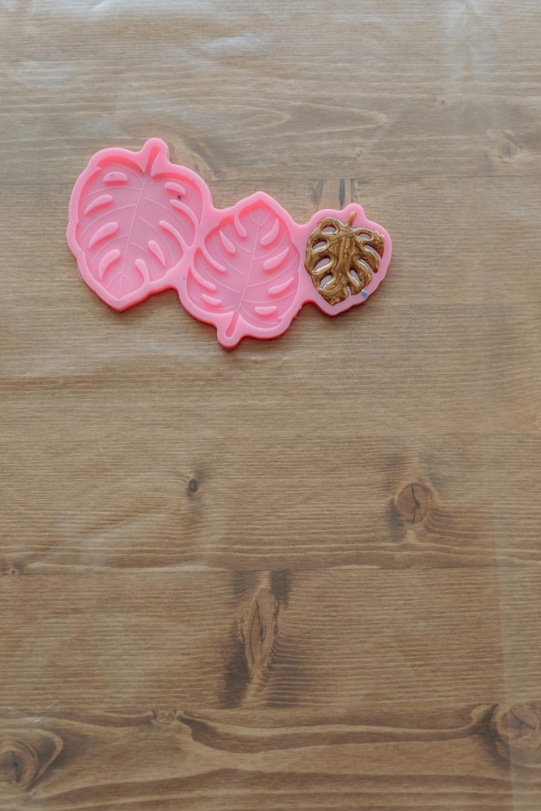 Pink silicone molds in leaf shapes lying on a wooden table, used for crafts. Moules en silicone roses en forme de feuilles posés sur une table en bois, utilisés pour des travaux manuels.